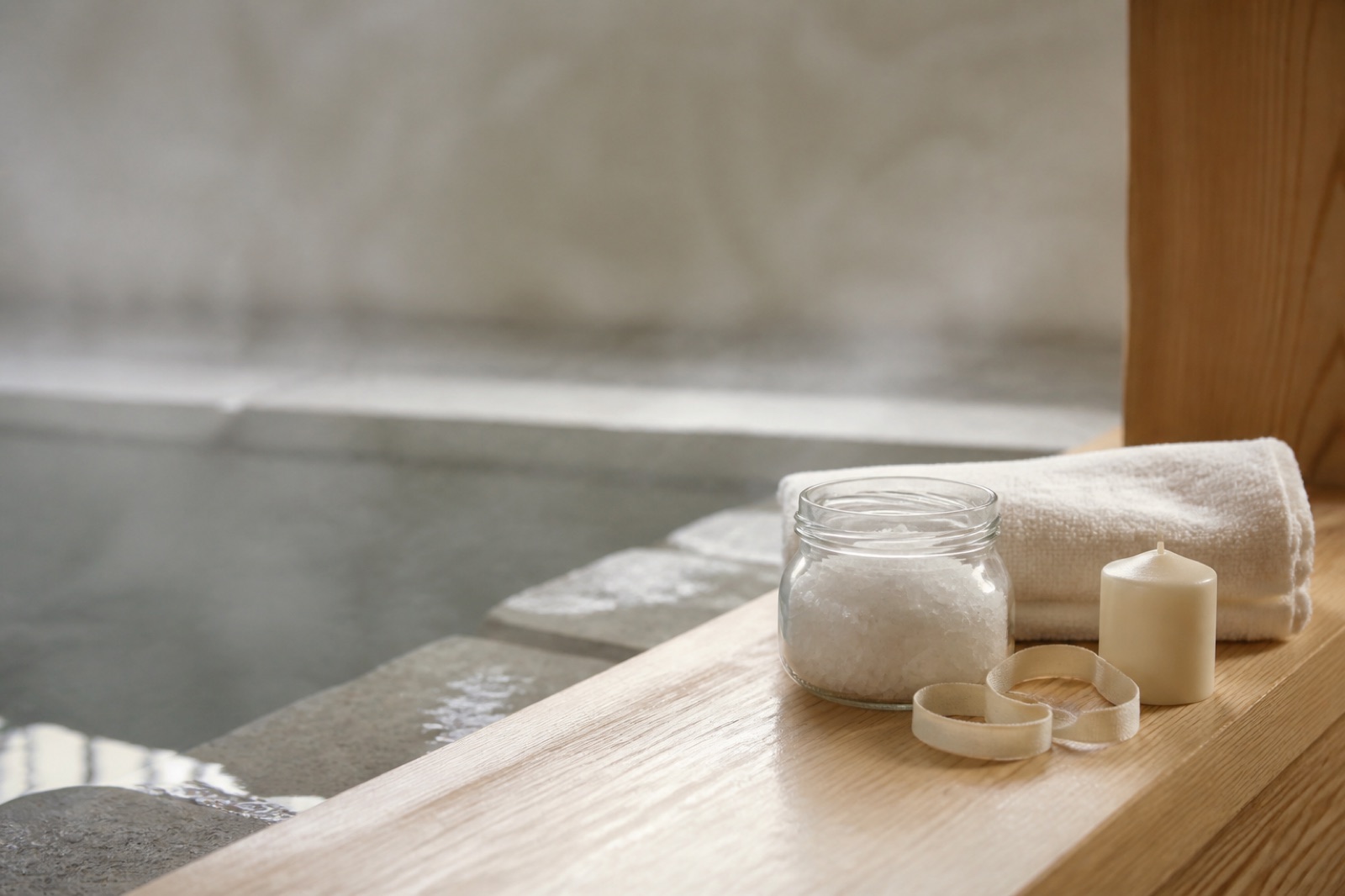 Inslagen present med badsalt i glasburk, vikt handduk och ett ljus på ljust trä