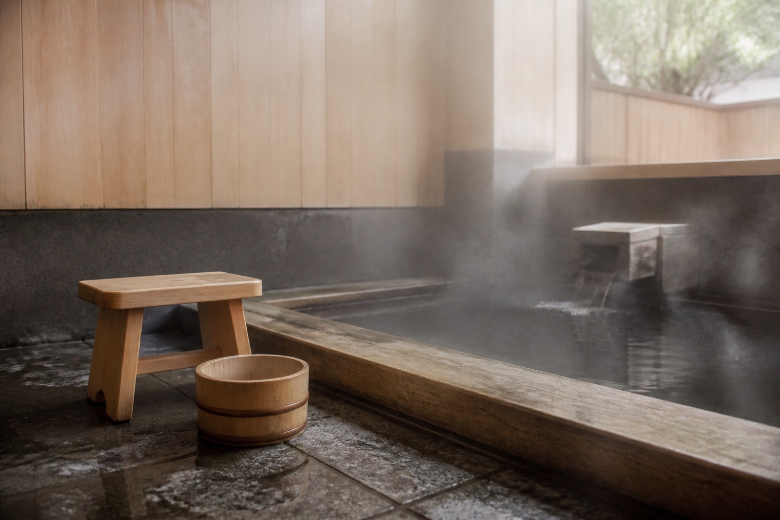 Träskopa och vattendroppar på ett vått stengolv — tvagningen som kommer före själva badet