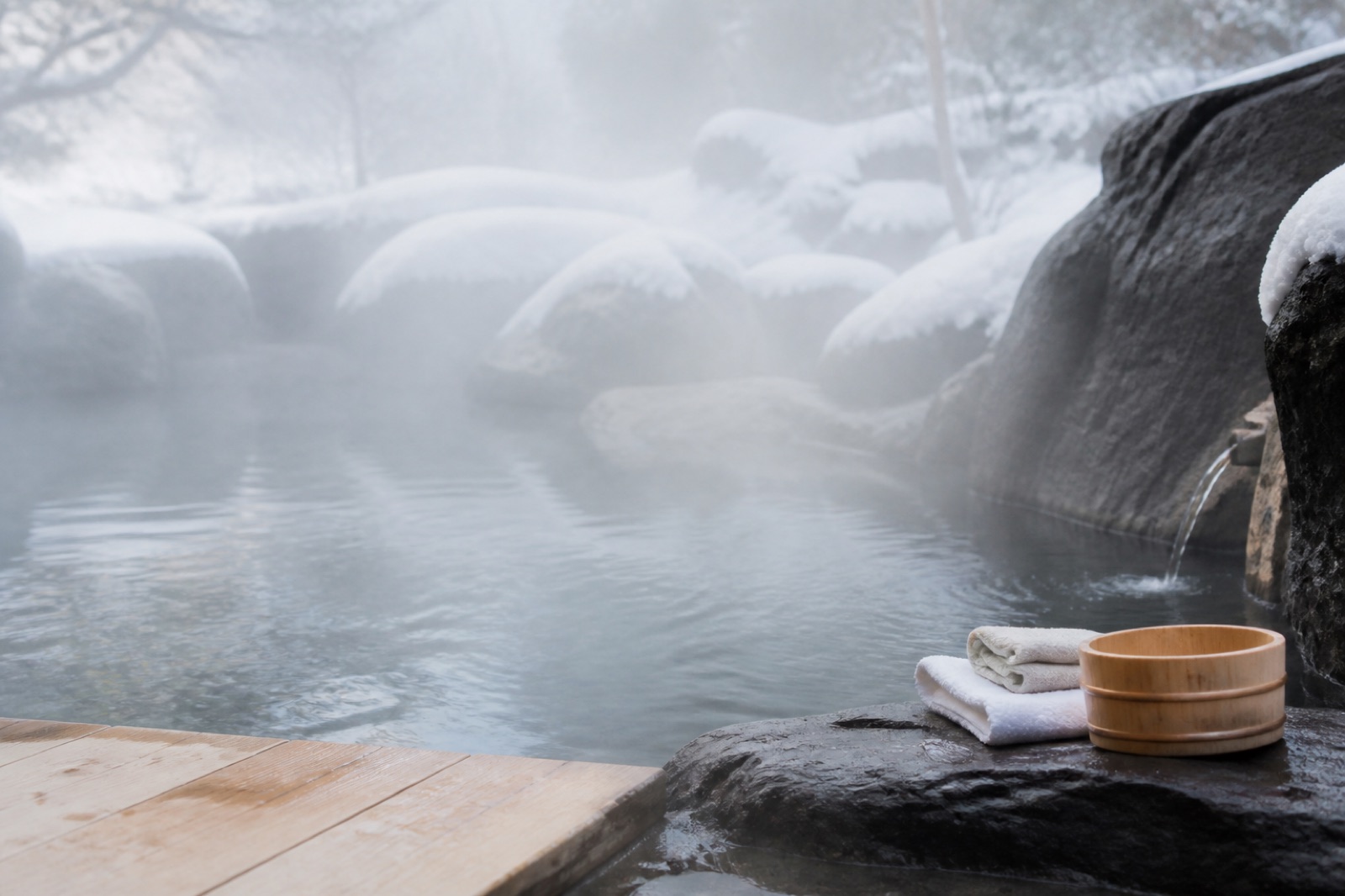 Utomhusbad med ångande naturligt källvatten omgivet av mörk våt sten och snö — en japansk onsen